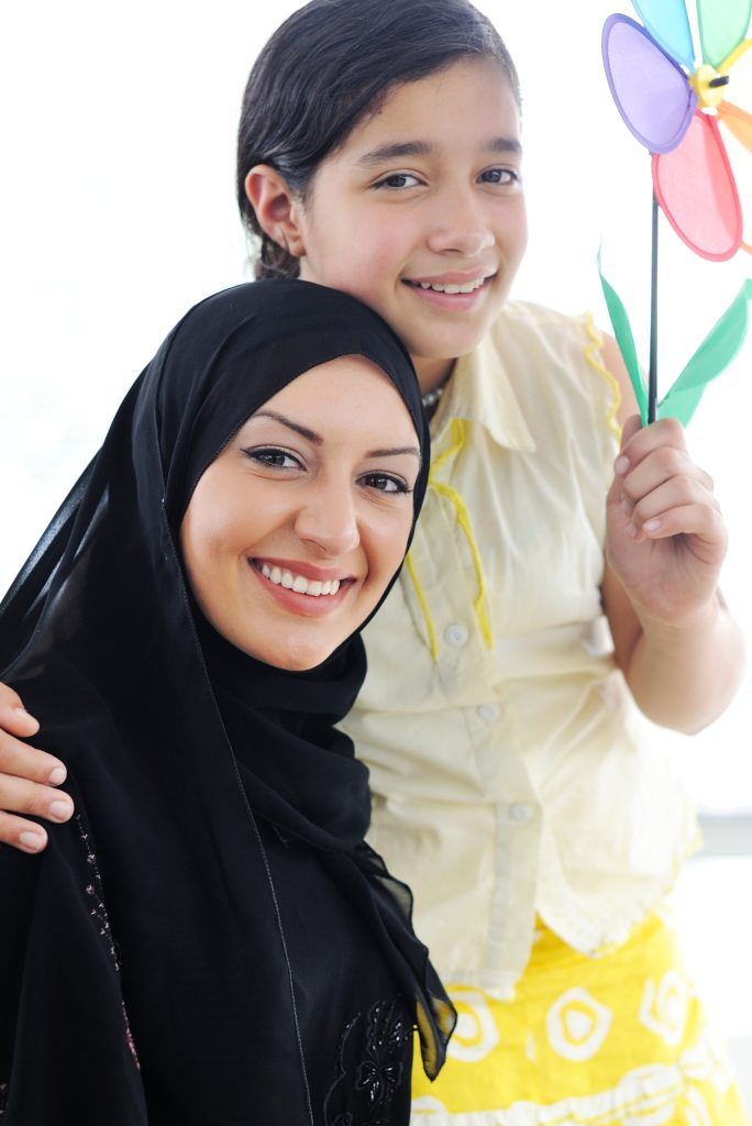 A photograph of a Muslim woman and her little daughter both smiling and facing the camera.